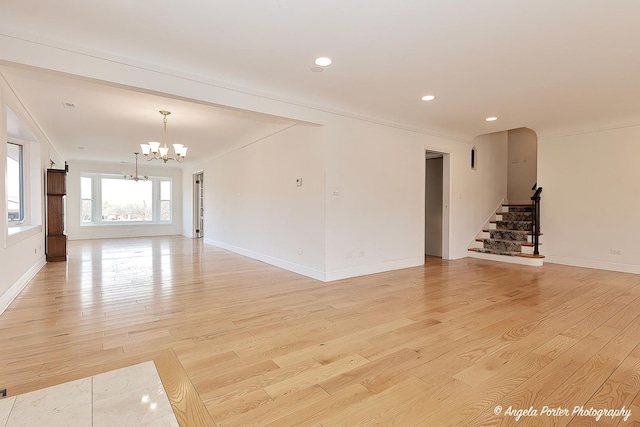 unfurnished living room featuring ornamental molding, an inviting chandelier, and light hardwood / wood-style flooring