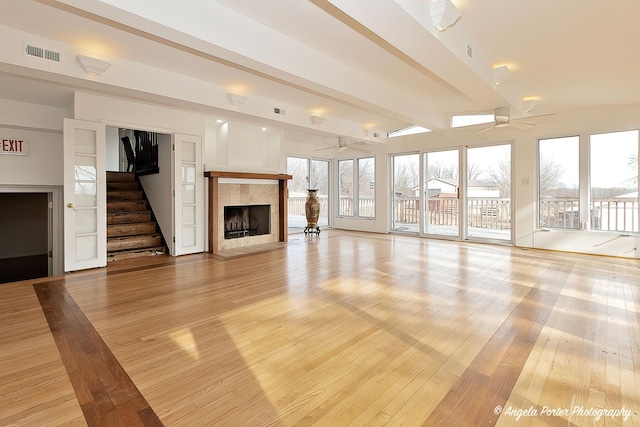 unfurnished living room featuring plenty of natural light, a tile fireplace, beamed ceiling, and ceiling fan