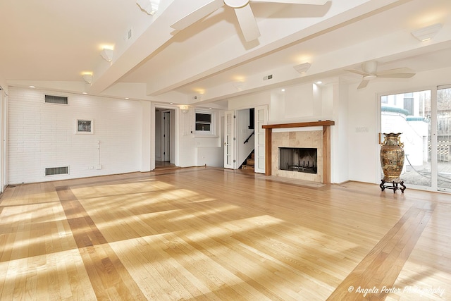 unfurnished living room with brick wall, hardwood / wood-style floors, a fireplace, ceiling fan, and beam ceiling