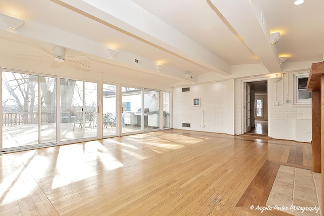 interior space with ceiling fan, light hardwood / wood-style flooring, beamed ceiling, and brick wall