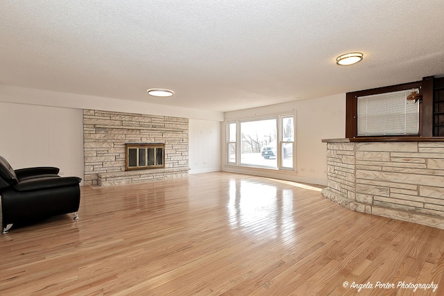 living room with a stone fireplace, a textured ceiling, and light wood-type flooring