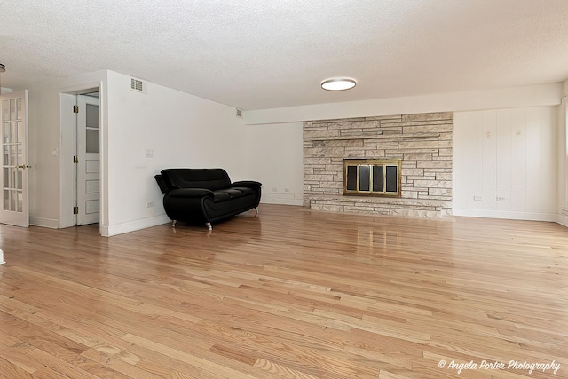 living room featuring a stone fireplace, light hardwood / wood-style flooring, and a textured ceiling