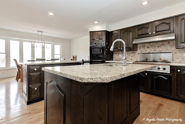 kitchen with light hardwood / wood-style flooring, hanging light fixtures, dark brown cabinetry, tasteful backsplash, and a center island with sink