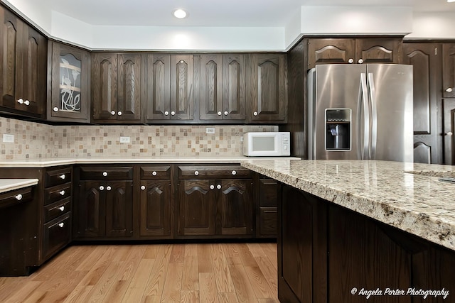 kitchen featuring decorative backsplash, stainless steel fridge, dark brown cabinetry, and light hardwood / wood-style flooring