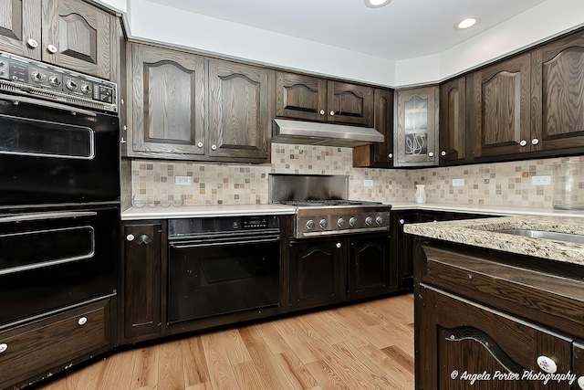 kitchen with black double oven, dark brown cabinetry, stainless steel gas cooktop, decorative backsplash, and light wood-type flooring