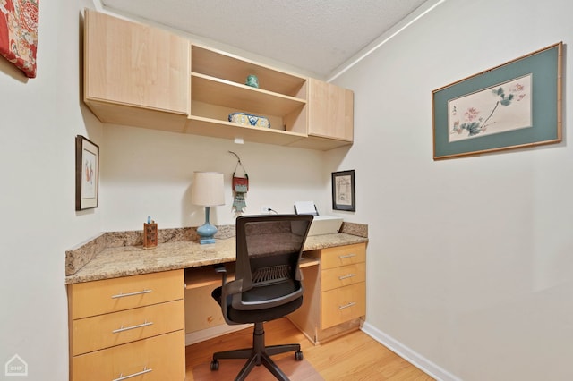 home office featuring light hardwood / wood-style flooring, built in desk, and a textured ceiling