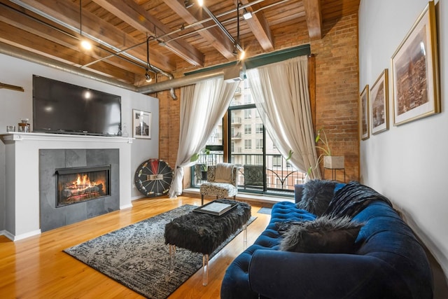 living room featuring brick wall, hardwood / wood-style floors, a fireplace, beamed ceiling, and wood ceiling