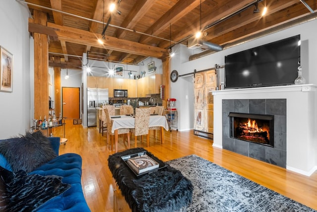 living room with beam ceiling, a fireplace, wooden ceiling, a barn door, and light wood-type flooring