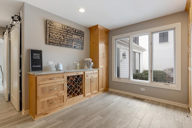 bar featuring light wood finished floors, a barn door, visible vents, and baseboards