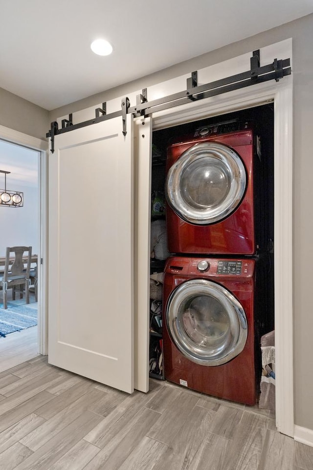 clothes washing area with stacked washer and dryer, a barn door, laundry area, and wood finished floors