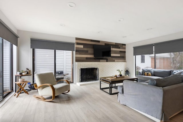 living area featuring an accent wall, light wood-type flooring, a fireplace, and recessed lighting