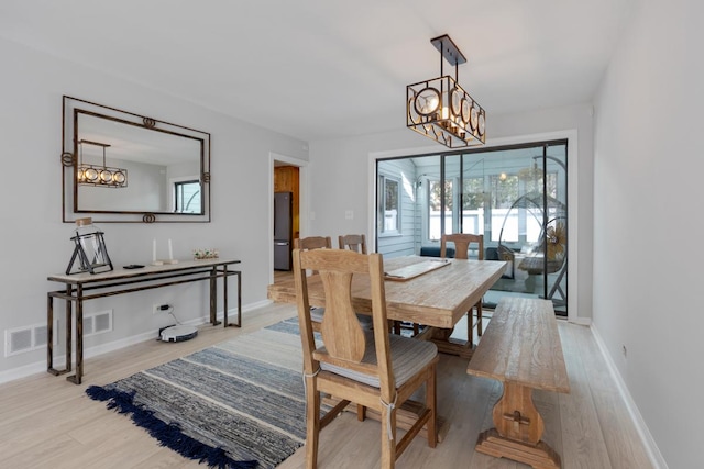 dining area featuring light wood-style floors, baseboards, visible vents, and a notable chandelier