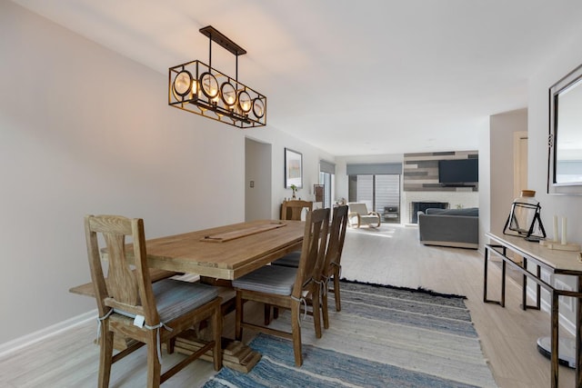 dining space with a chandelier, light wood-type flooring, a fireplace, and baseboards