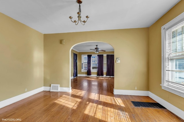 empty room featuring hardwood / wood-style flooring, plenty of natural light, and ceiling fan with notable chandelier