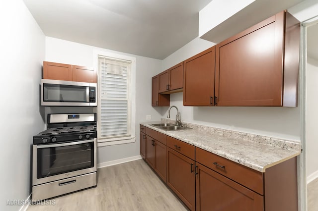 kitchen featuring light stone counters, appliances with stainless steel finishes, light hardwood / wood-style floors, and sink