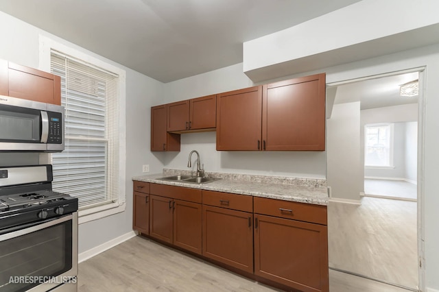 kitchen with light stone countertops, appliances with stainless steel finishes, sink, and light hardwood / wood-style flooring