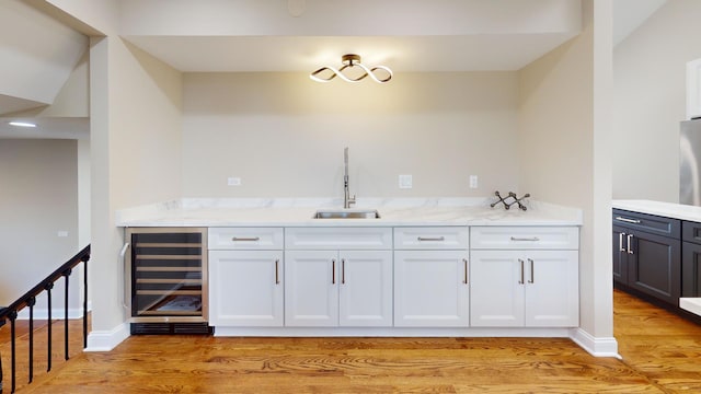 kitchen with sink, wine cooler, light stone counters, light hardwood / wood-style floors, and white cabinets