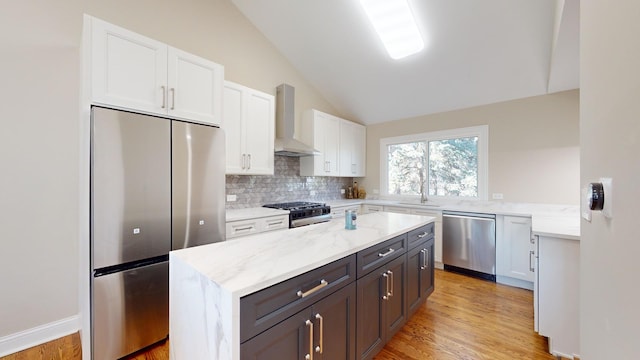 kitchen featuring appliances with stainless steel finishes, white cabinets, a kitchen island, vaulted ceiling, and wall chimney exhaust hood