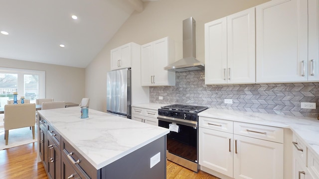 kitchen featuring stainless steel fridge, white cabinets, a kitchen island, gas range, and wall chimney exhaust hood