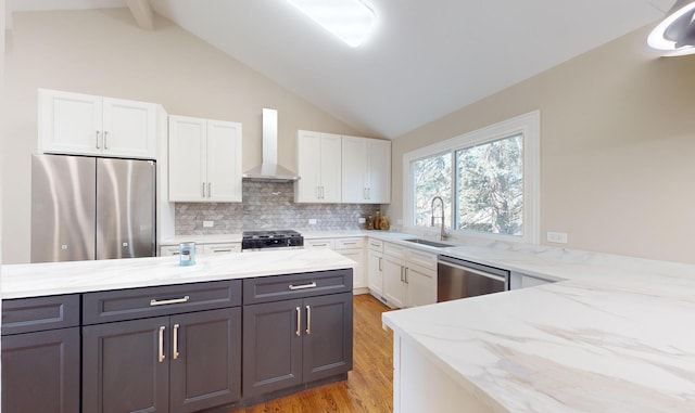 kitchen featuring appliances with stainless steel finishes, sink, white cabinets, light stone counters, and wall chimney exhaust hood