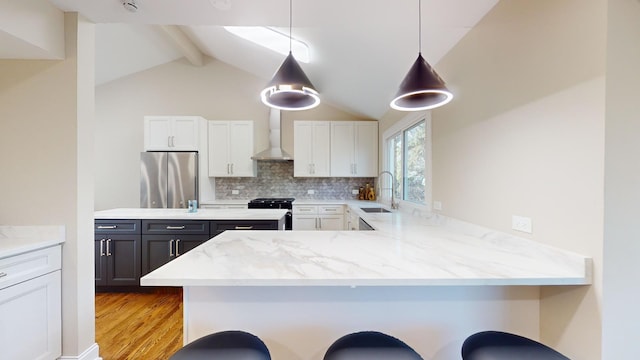 kitchen featuring pendant lighting, sink, kitchen peninsula, stainless steel appliances, and wall chimney range hood