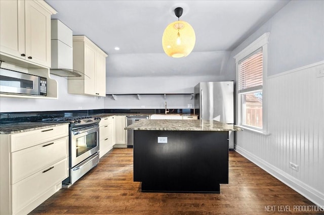 kitchen featuring a kitchen island, appliances with stainless steel finishes, pendant lighting, dark stone countertops, and wall chimney range hood