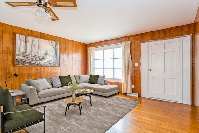 living room featuring ceiling fan, light wood-type flooring, and wood walls