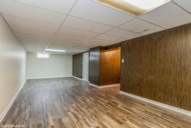 basement featuring a paneled ceiling, dark hardwood / wood-style floors, and wood walls