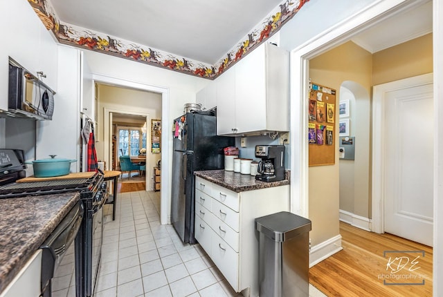 kitchen featuring white cabinets, dark stone countertops, light tile patterned floors, and black appliances