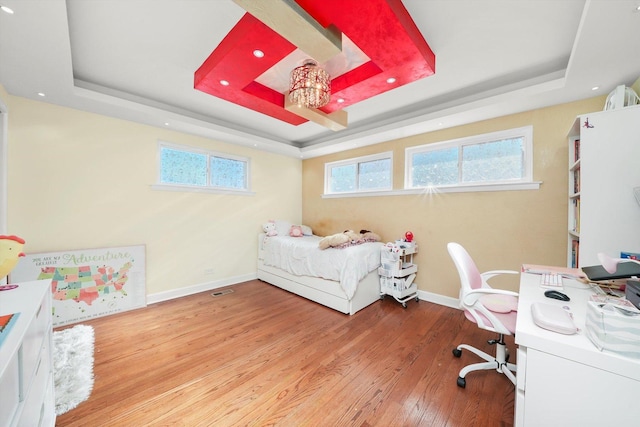 bedroom with light wood-type flooring and a tray ceiling