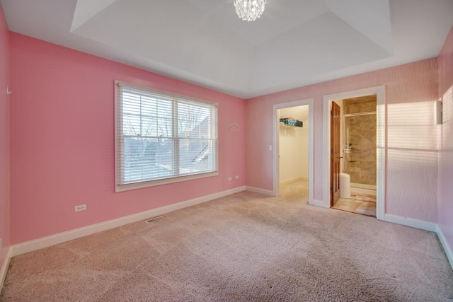 unfurnished bedroom with ensuite bathroom, a spacious closet, a raised ceiling, carpet floors, and a notable chandelier