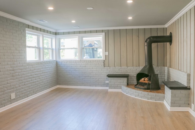 unfurnished living room featuring visible vents, brick wall, ornamental molding, a wood stove, and wood finished floors