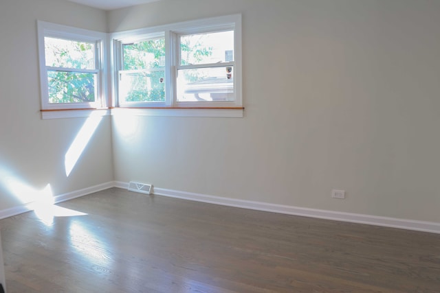 empty room featuring dark wood finished floors, visible vents, and baseboards