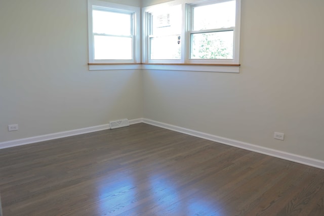 empty room with a wealth of natural light, visible vents, baseboards, and dark wood-style floors