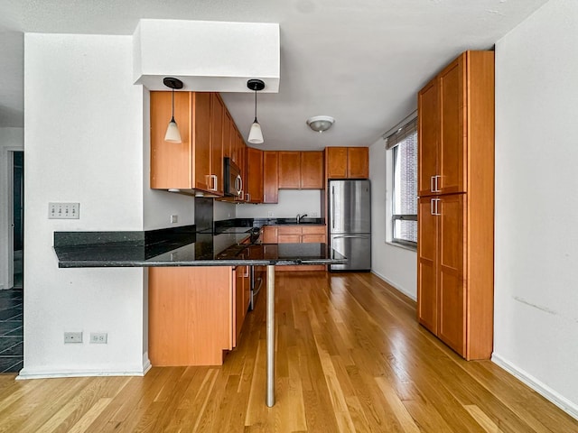 kitchen featuring pendant lighting, light hardwood / wood-style flooring, a breakfast bar, stainless steel appliances, and kitchen peninsula