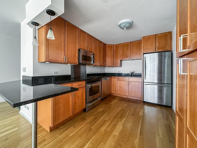 kitchen featuring decorative light fixtures, a breakfast bar area, kitchen peninsula, stainless steel appliances, and light wood-type flooring