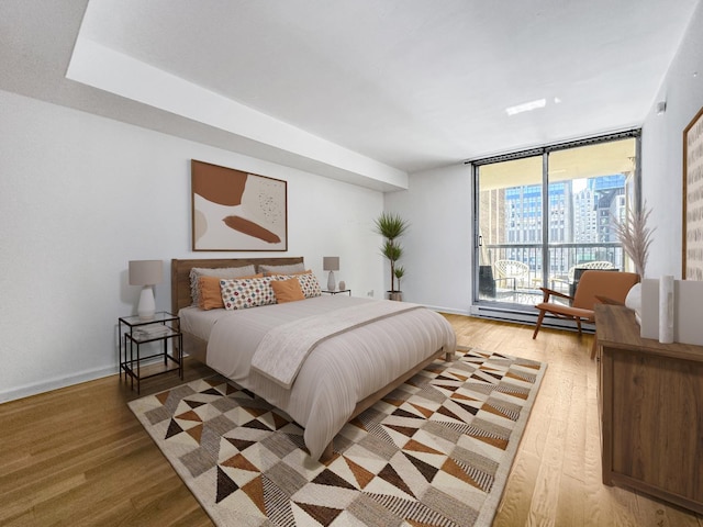 bedroom featuring a baseboard heating unit, access to outside, light wood-type flooring, and a wall of windows