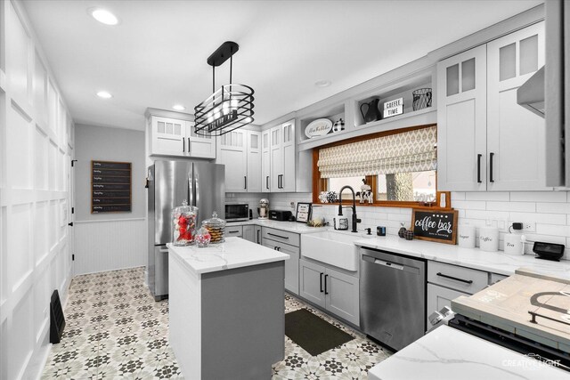 kitchen featuring light stone counters, stainless steel appliances, recessed lighting, wainscoting, and a sink