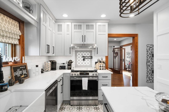 kitchen featuring recessed lighting, under cabinet range hood, appliances with stainless steel finishes, decorative backsplash, and glass insert cabinets