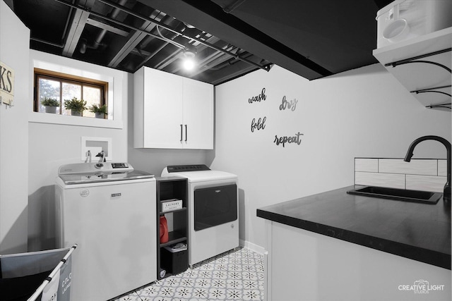 clothes washing area with a sink, cabinet space, light floors, and washer and dryer