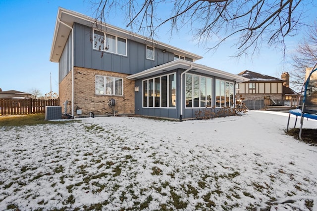 snow covered property with central AC, a sunroom, and a trampoline