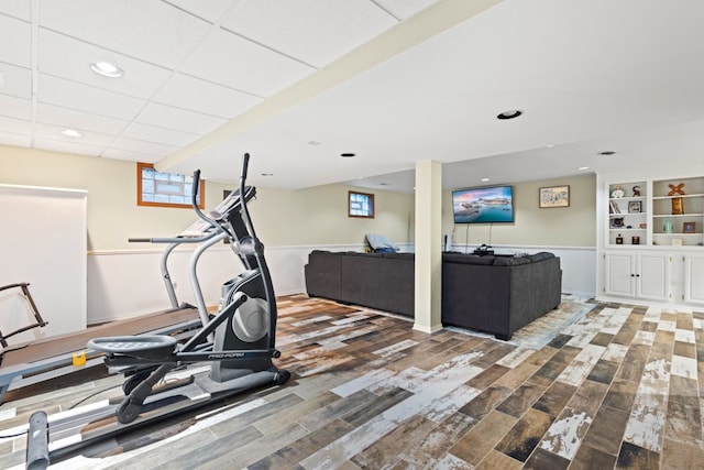 exercise area with a drop ceiling, wood-type flooring, and a healthy amount of sunlight