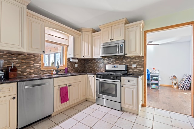 kitchen featuring appliances with stainless steel finishes, sink, dark stone countertops, light tile patterned floors, and cream cabinetry