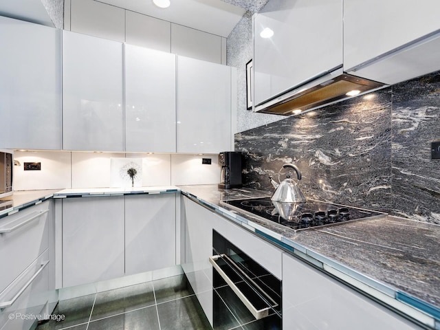 kitchen featuring exhaust hood, tasteful backsplash, black appliances, dark tile patterned flooring, and white cabinets