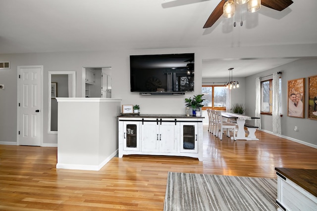 unfurnished living room with beverage cooler, ceiling fan with notable chandelier, and light wood-type flooring