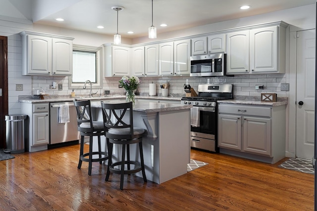 kitchen with a kitchen island, appliances with stainless steel finishes, pendant lighting, a breakfast bar area, and dark wood-type flooring