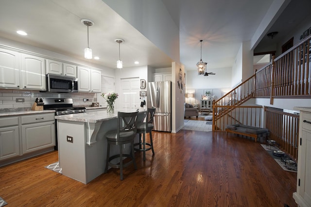 kitchen featuring dark wood-type flooring, appliances with stainless steel finishes, white cabinetry, a center island, and decorative light fixtures