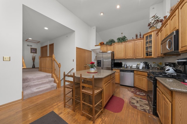 kitchen with stainless steel appliances, a center island, light hardwood / wood-style flooring, and dark stone counters