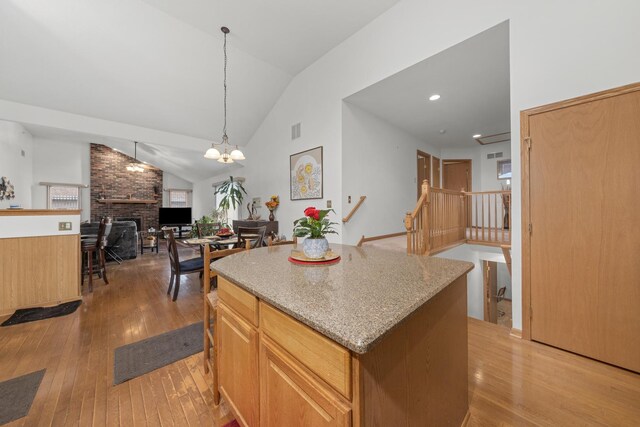 kitchen with pendant lighting, high vaulted ceiling, a fireplace, a center island, and light wood-type flooring