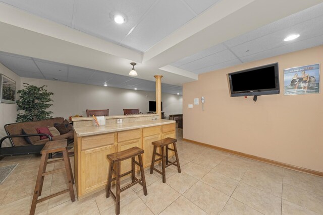 kitchen with a kitchen bar, a paneled ceiling, light tile patterned flooring, and light brown cabinets